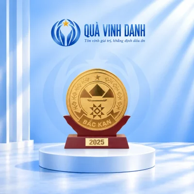 Biểu trưng mặt đồng tròn màu vàng trên đế gỗ đỏ sẫm và bục trắng Quà Vinh Danh