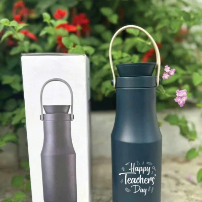 Ảnh nguồn bình xanh có chữ Happy Teachers’ Day cạnh hộp in METRO DOUBLE TUMBLER ngoài trời