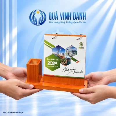 Bối cảnh minh họa các bàn tay trao bộ lịch đế gỗ và ống bút, giữ SMI, hai khoen và toàn bộ tờ bìa năm 2024