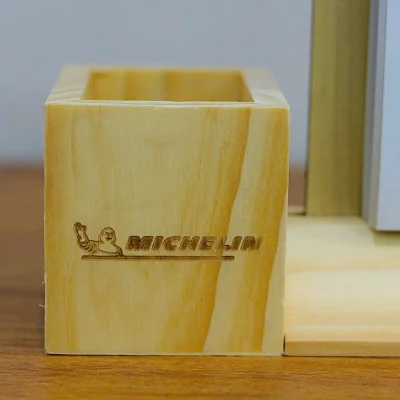 Ảnh chụp thật cận ống bút vuông giữ nhân vật, chữ MICHELIN, đường gạch dưới, vân gỗ và miệng mở