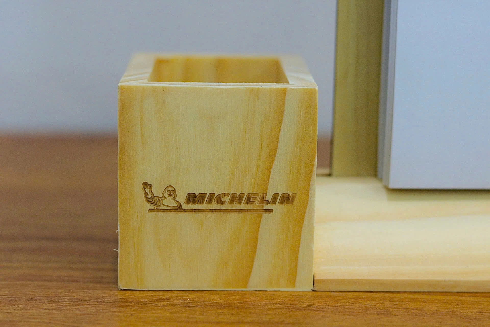 Ảnh chụp thật cận ống bút vuông giữ nhân vật, chữ MICHELIN, đường gạch dưới, vân gỗ và miệng mở