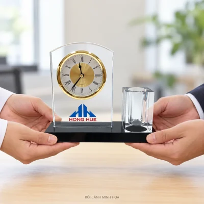 Bối cảnh minh họa bàn tay trao bộ pha lê đồng hồ và ống bút trống trên đế đen, giữ HONG HUE và biểu trưng xanh