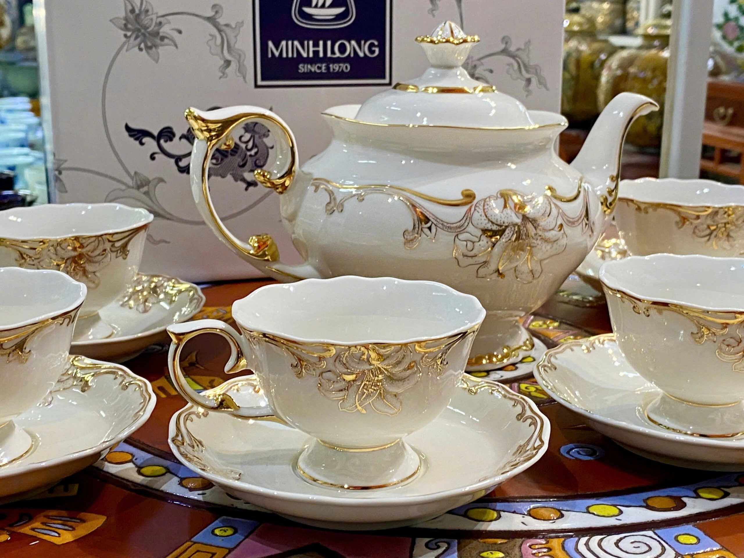 Ảnh nguồn cận chén Đài Các có chân, miệng lượn, quai uốn và đĩa hoa văn, giữ chữ MINHLONG SINCE 1970 trên hộp
