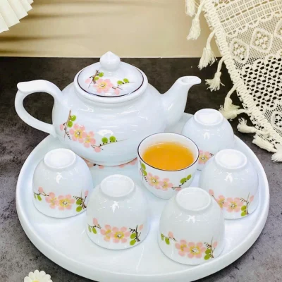 Ảnh chụp nguồn bộ hoa màu hồng gồm một ấm, năm chén úp, một chén ngửa và khay sứ tròn, giữ toàn khung