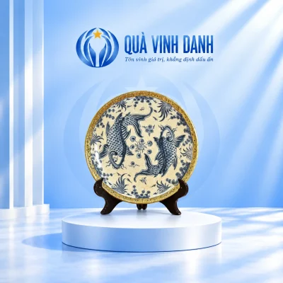 Đĩa biểu trưng bọc đồng mặt hai cá chép xanh nền ngà, viền hoa văn màu vàng và đế gỗ trên bục Quà Vinh Danh
