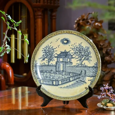 Ảnh chụp nguồn đĩa bọc đồng có cảnh lầu các, cây và mặt nước với viền hoa văn màu vàng