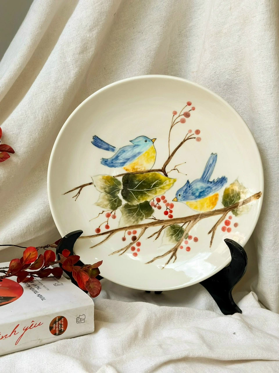 Ảnh chụp nguồn mặt hai chim xanh vàng trên cành, lá và quả đỏ với đế đen, giữ nguyên họa tiết