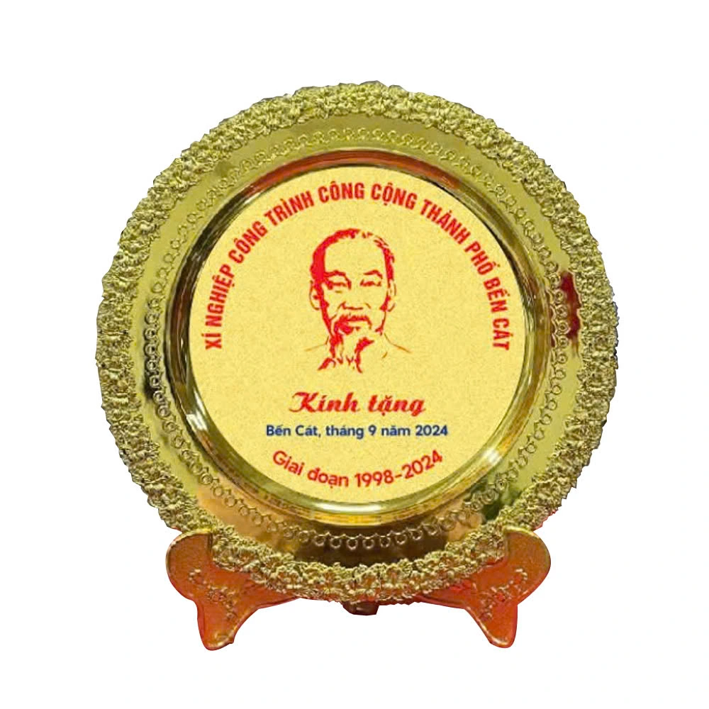 Ảnh thật đĩa mạ vàng có chân dung, tên Xí nghiệp Công trình Công cộng thành phố Bến Cát và giai đoạn 1998–2024, giữ nguyên chữ nguồn