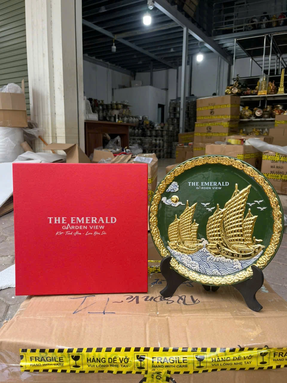 Ảnh chụp nguồn đĩa thuyền buồm nền xanh và hộp đỏ, giữ nguyên chữ THE EMERALD GARDEN VIEW cùng các thông tin gốc
