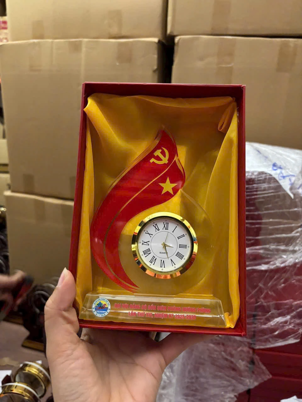Ảnh chụp thật nguồn đồng hồ ngọn lửa hai dải trong hộp đỏ lót vàng, giữ tên Hướng Phùng và nhiệm kỳ 2025–2030