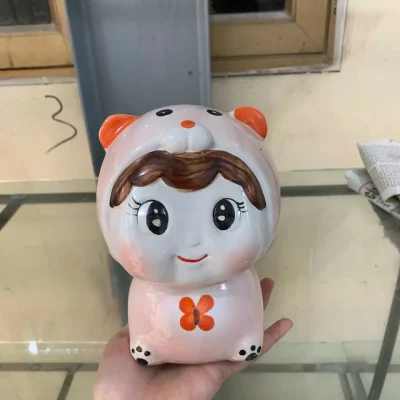 Ảnh nguồn búp bê hồng nhạt trên tay, thấy mái tóc nâu, mắt cười và cánh bướm cam
