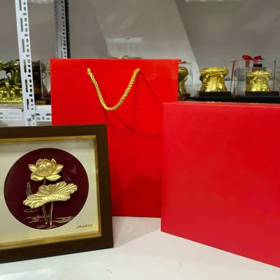 Ảnh nguồn tranh hoa sen nền đỏ đặt cạnh hộp và túi quà màu đỏ để tham khảo cách bao gói