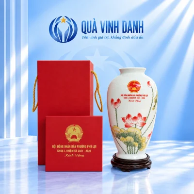 Lọ hoa đùi dế men trắng vẽ sen đỏ trên đế tròn cạnh hộp đỏ, nền Quà Vinh Danh