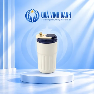 Ly giữ nhiệt thân kem rãnh dọc nắp xanh đậm màn hình tròn chi tiết trắng núm vàng trên bục nền Quà Vinh Danh