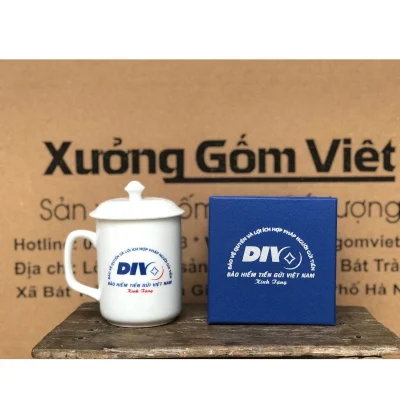 Ảnh chụp ly quai vuông có nắp và hộp xanh giữ biểu trưng DIV, Bảo hiểm Tiền gửi Việt Nam cùng Kính Tặng