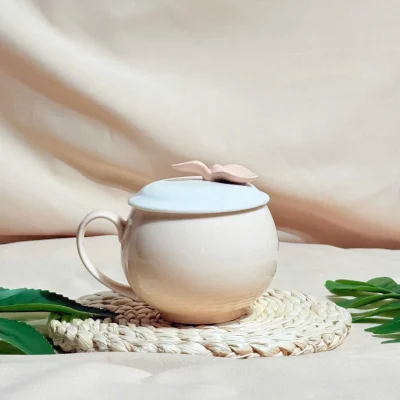 Ảnh thật nguồn ly táo kem trơn có quai trái, nắp xanh nhạt và núm lá be hồng trên tấm đan