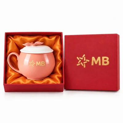 Ảnh nguồn đã xử lý: ly táo hồng nắp trắng mang chữ MB trong hộp đỏ lót cam, nắp hộp cũng có MB