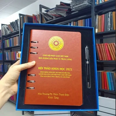 Ảnh thật nguồn sổ còng hở màu nâu trong hộp xanh cùng bút, giữ nội dung Giáo hội Phật giáo Việt Nam, hội thảo 2021, tên và Kính Tặng