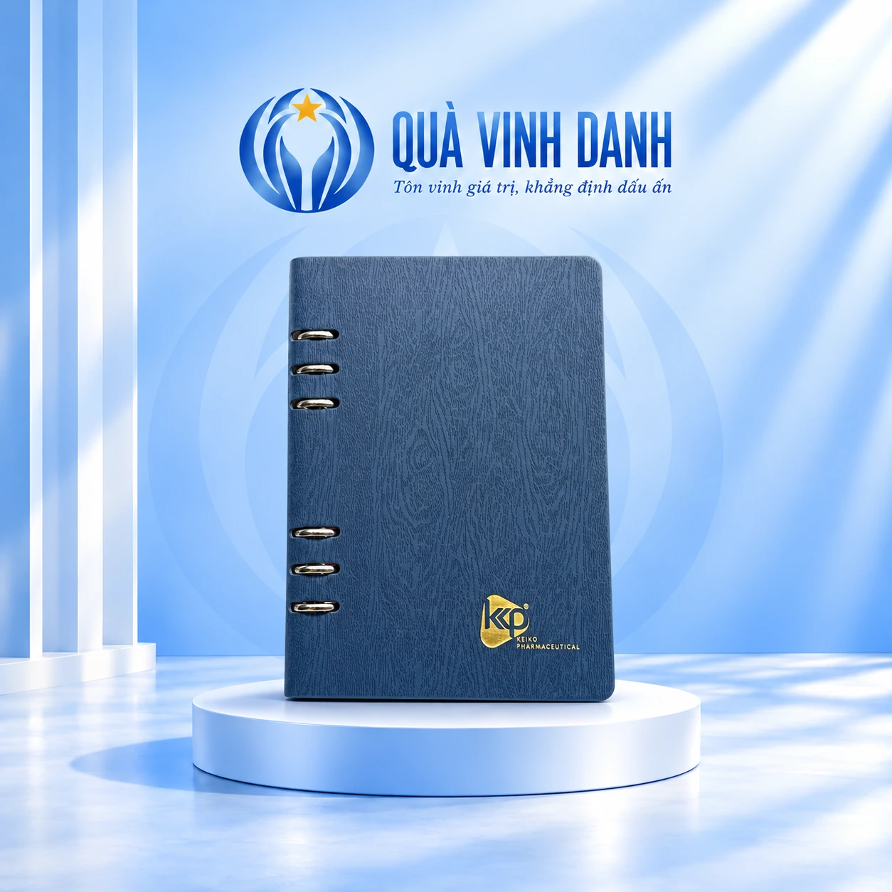 Minh họa sổ còng hở A5-02 xanh xám trên bục Quà Vinh Danh, giữ sáu còng ngoài và logo KP KEIKO PHARMACEUTICAL