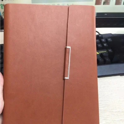 Ảnh thật nguồn sổ SC01 màu nâu được cầm trước bàn làm việc, giữ bề mặt trống và chi tiết đứng màu bạc