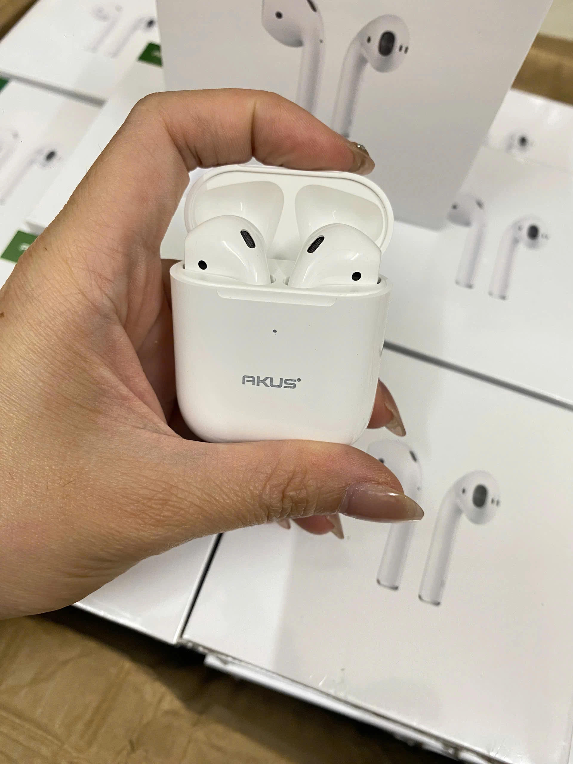 Ảnh chụp nguồn hộp AKUS A2 trắng mở trong tay có hai tai nghe bên trong chấm nhỏ phía trước logo hãng và các hộp nền giữ nguyên khung