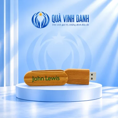 Ảnh đổi nền USB gỗ xoay UGV 007 mở gần thẳng giữ chữ John Lewis xanh trên ốp dài bên trái thân gỗ và đầu USB bên phải trên bục Quà Vinh Danh